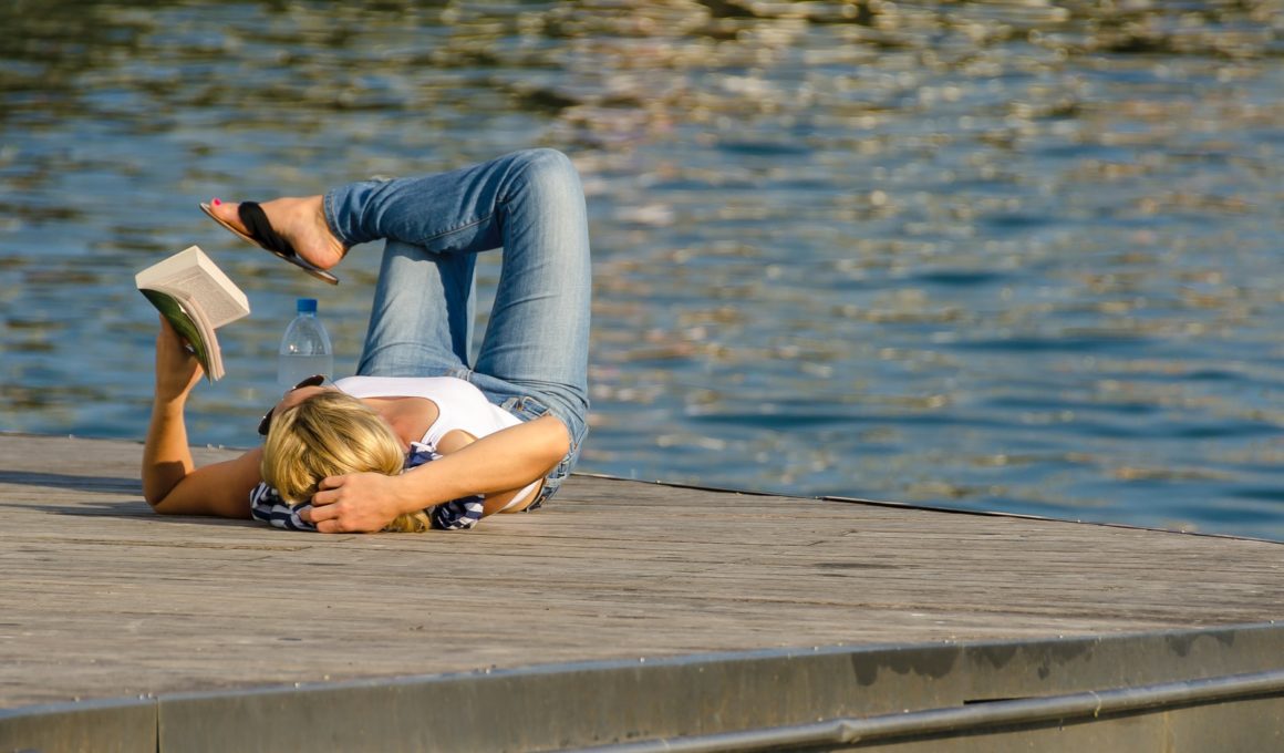 woman in white tank top and gray pants lying on brown wooden dock during daytime